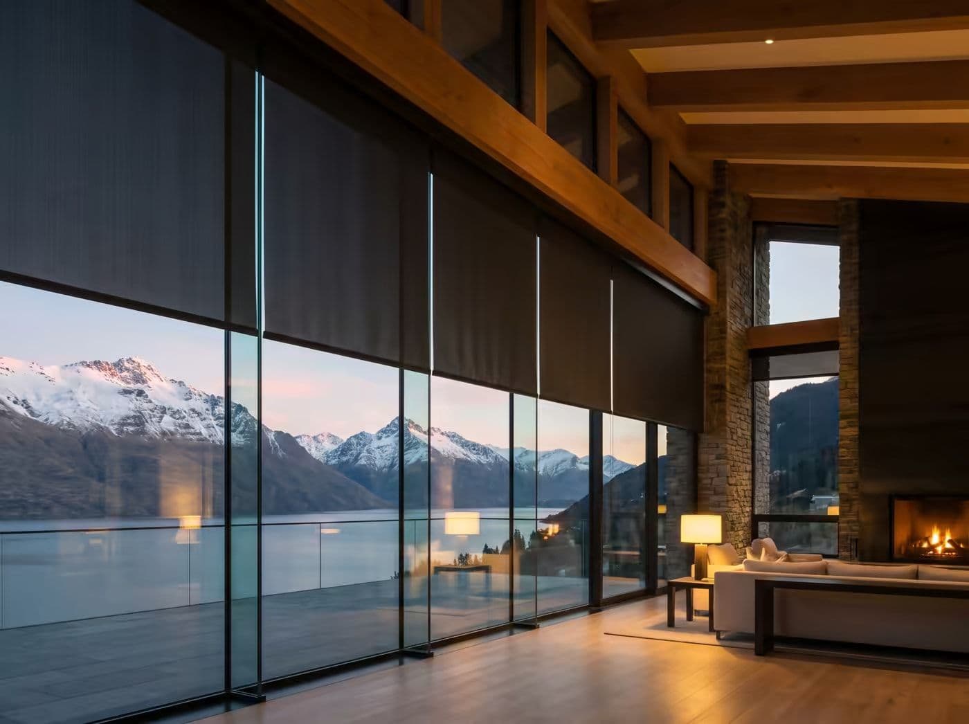 Motorized shades lowering over a mountain window wall at dusk