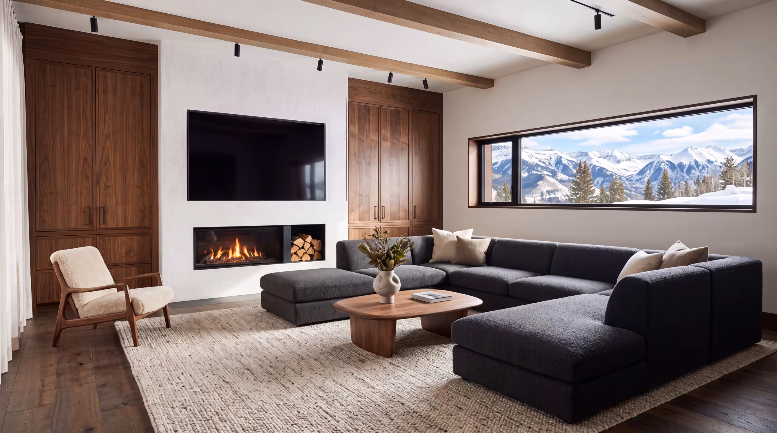A finished mountain-modern great room: a large screen set flush into the plaster above a linear fireplace, a sectional, and a window onto the peaks. Nothing else of the system is visible.